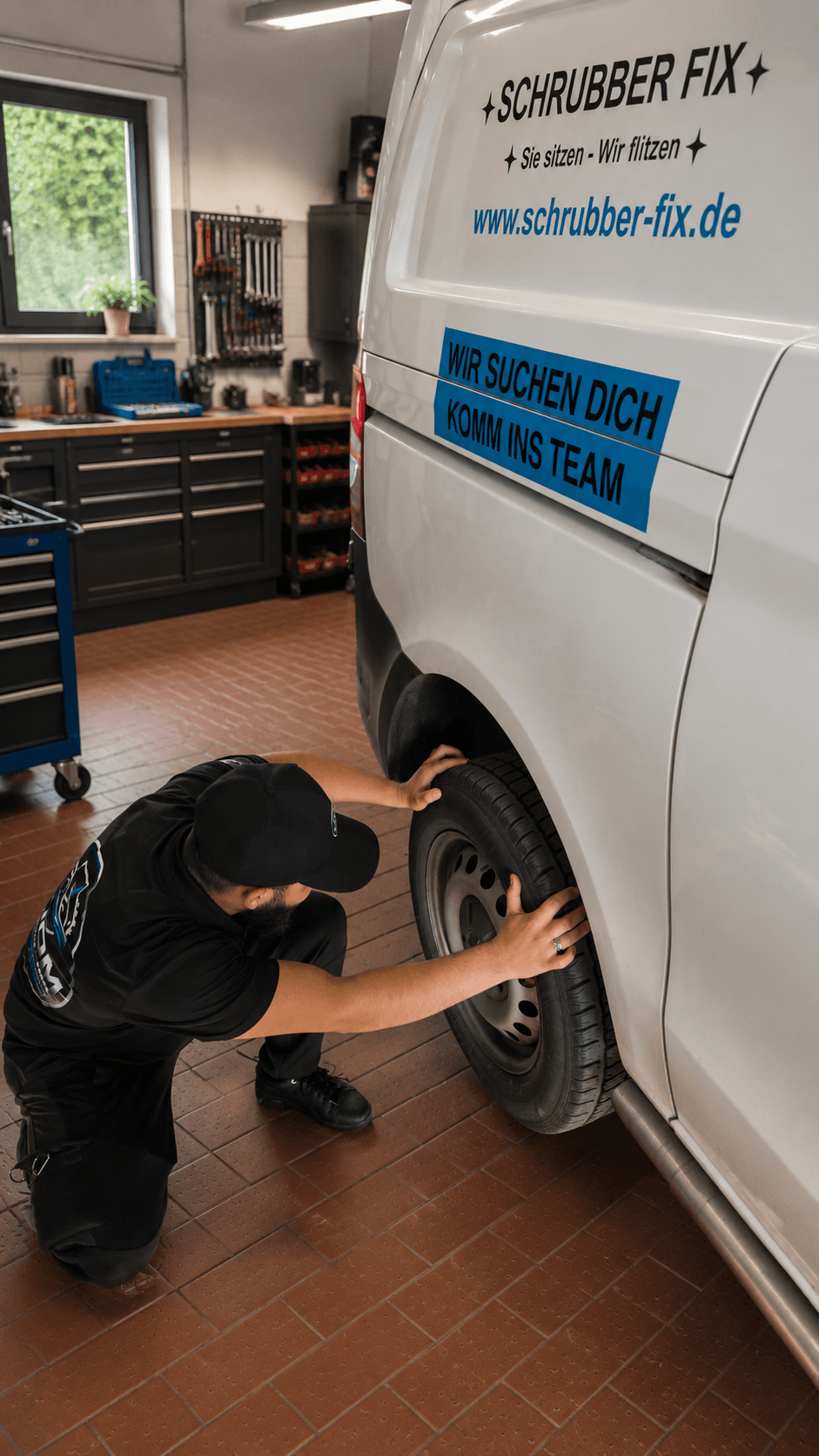 Ein Mechaniker kniet in einer Werkstatt und arbeitet am Reifen eines weißen Schrubber Fix Transporters.
