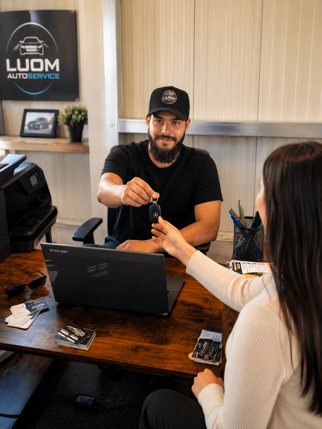 Ein Mitarbeiter von LUOM Autoservice übergibt einer Kundin an einem Schreibtisch die Autoschlüssel.